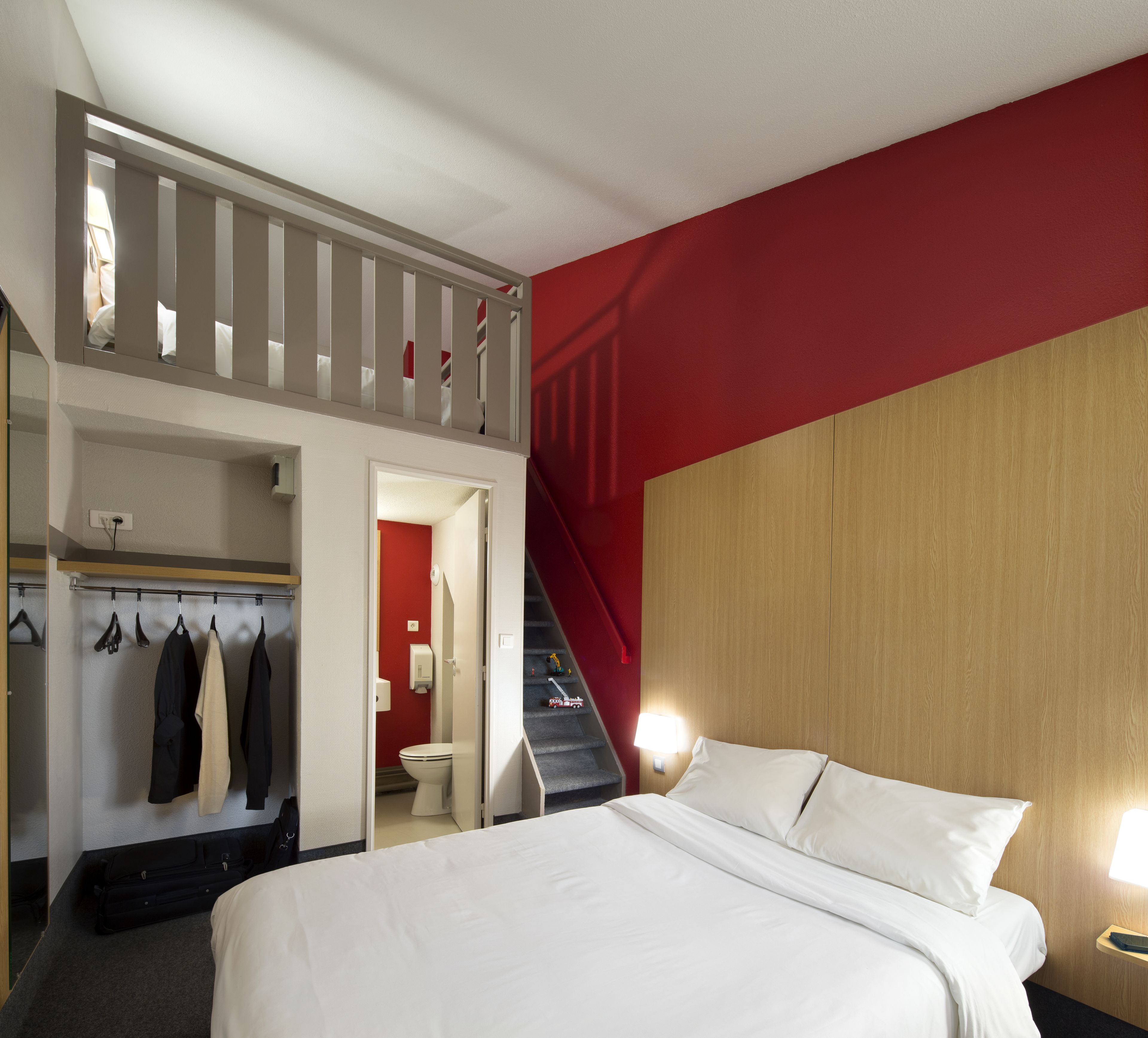 A hotel room with a bed, a closet with hanging clothes, a staircase, and a bathroom.