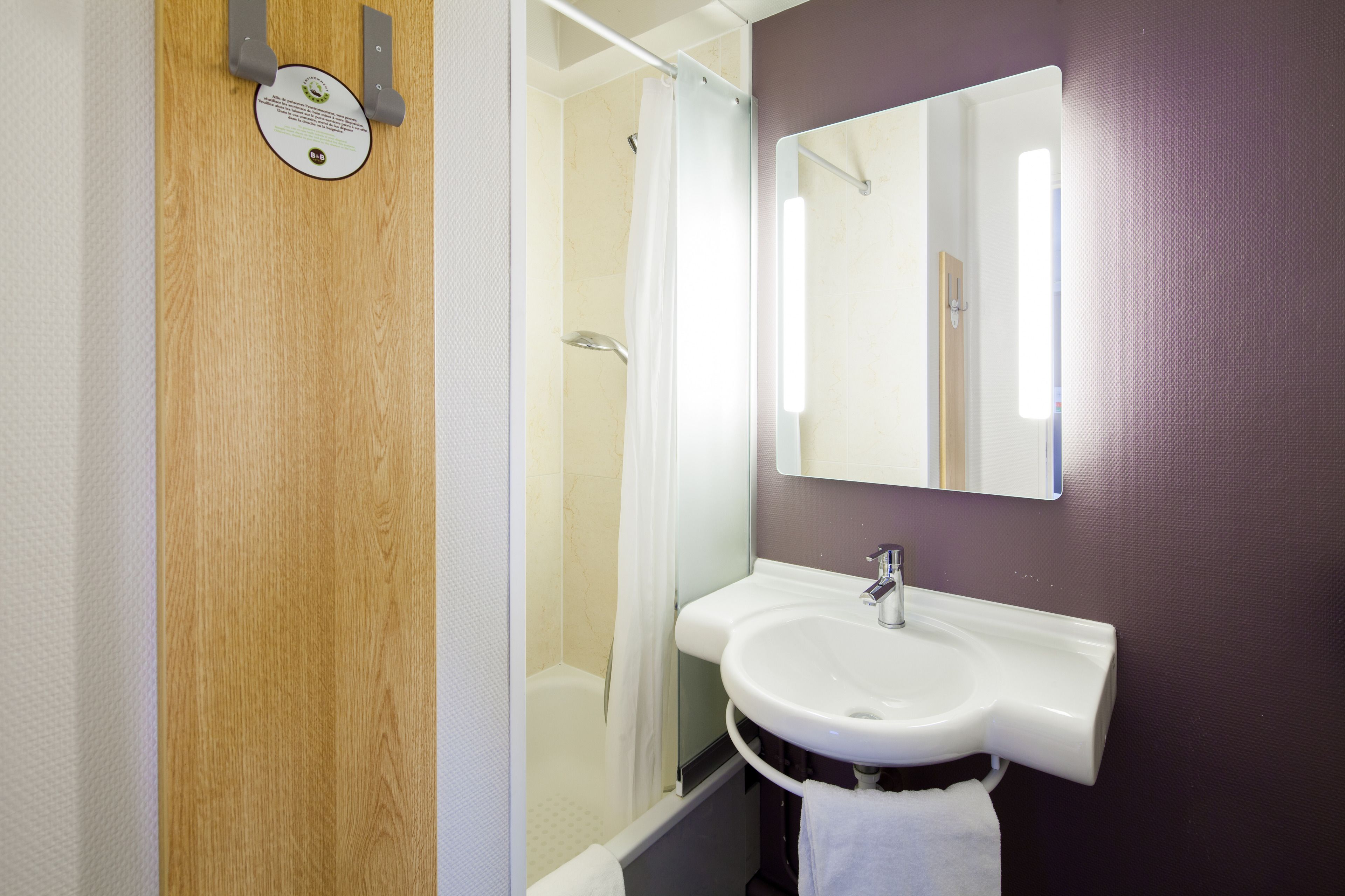 Un baño con puerta de madera, un lavabo blanco, un espejo y una ducha.