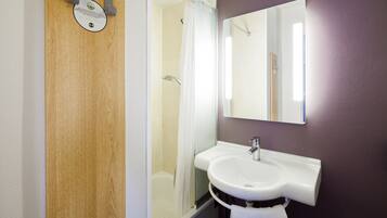 A bathroom with a wooden door, a white sink, a mirror, and a shower.