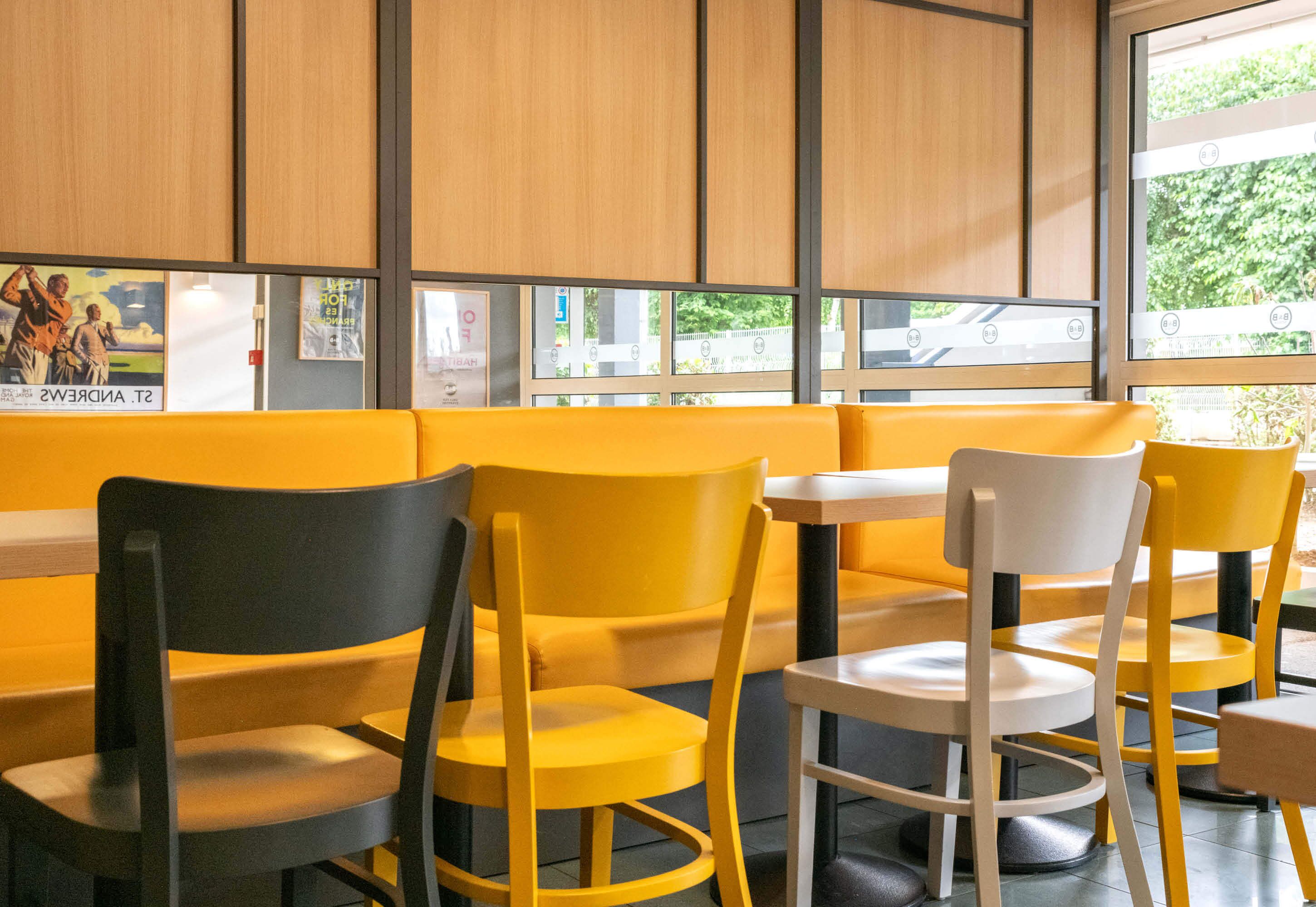 Un área de descanso con sillas y un banco amarillo y blanco, paredes de paneles de madera y vistas al exterior.