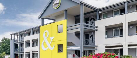 A modern hotel with a prominent yellow and white sign, multiple balconies, and a welcoming entrance.