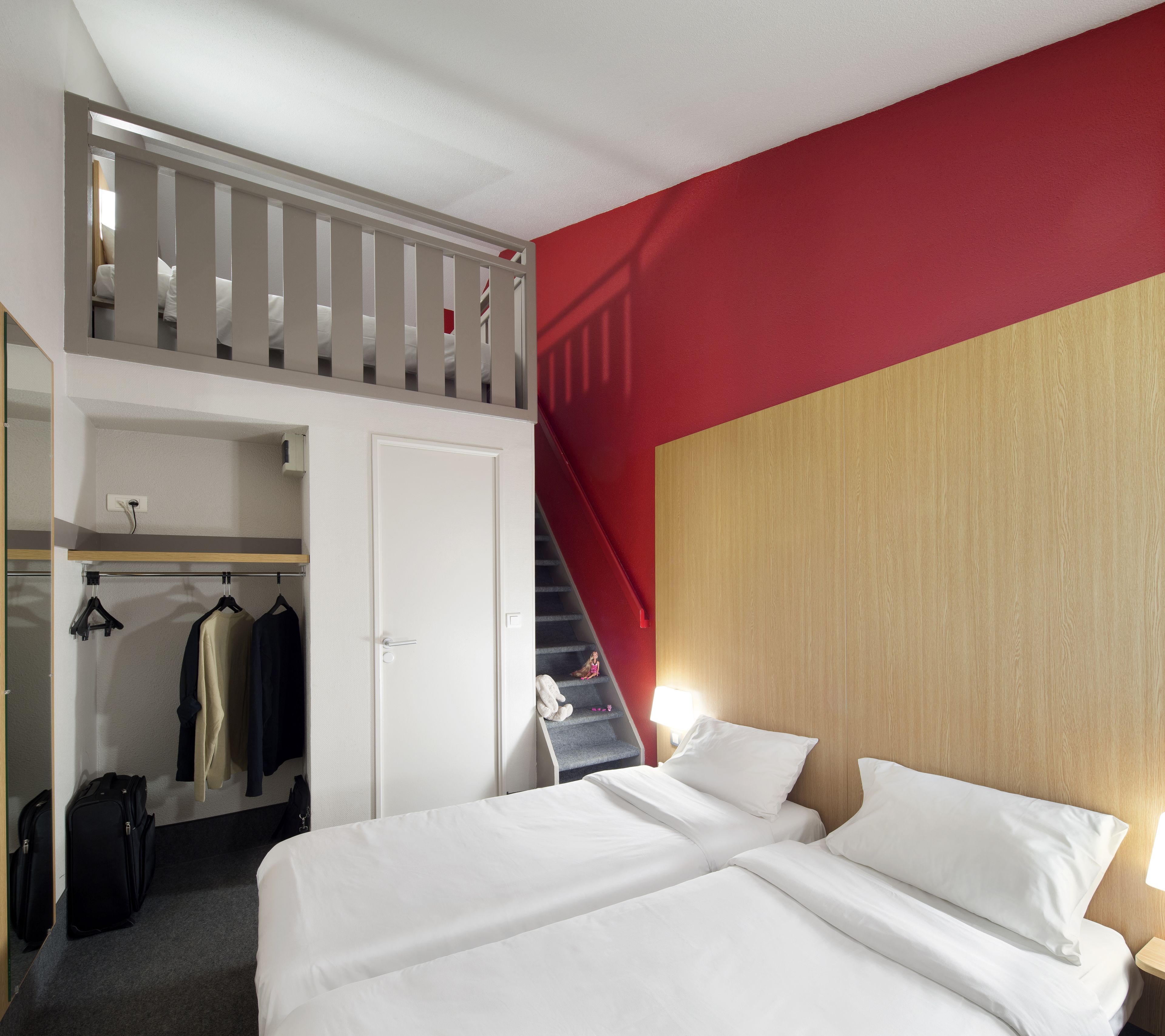 Une chambre d’hôtel avec un lit en mezzanine, une armoire et un escalier.
