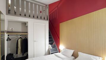 Une chambre d’hôtel avec un lit en mezzanine, une armoire et un escalier.