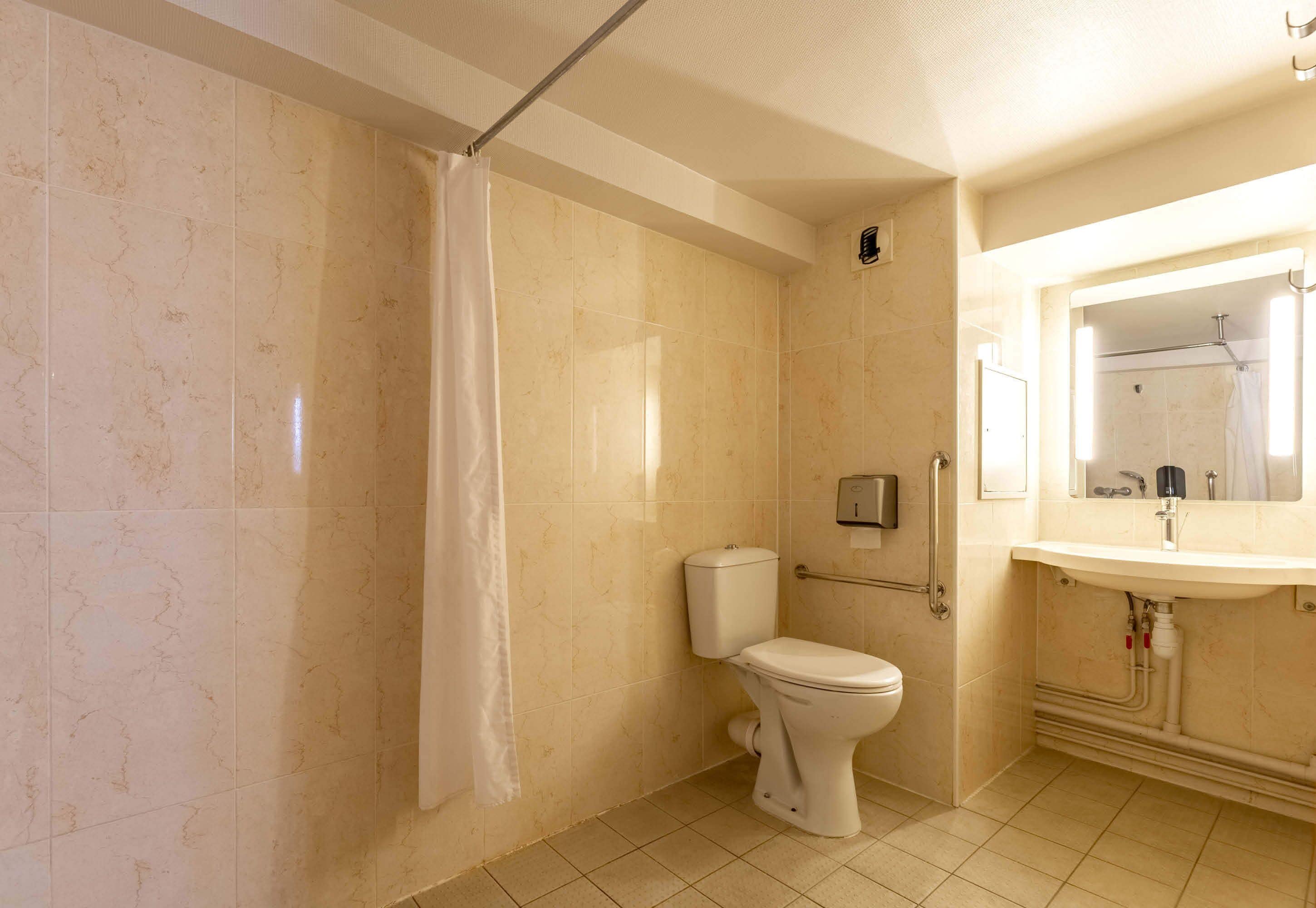 A bathroom with a toilet, a shower curtain, a hand dryer, and a sink with a mirror.
