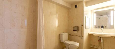 A bathroom with a toilet, a shower curtain, a hand dryer, and a sink with a mirror.