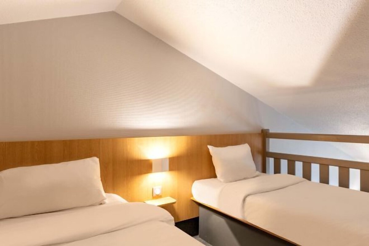 Habitación de hotel con dos camas, cabecera de madera y mesita de noche con lámpara.
