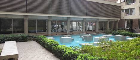 A modern building with a rooftop pool area, surrounded by greenery and featuring large windows and balconies.