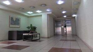 A lobby with a reception desk, a potted plant, a framed picture on the wall, and an elevator in the background. - Alojamientos Santiago Chile (Santiago)