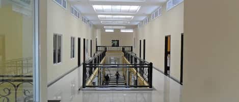 Un corredor amplio y luminoso con una escalera central, suelos de baldosas y un diseño moderno.