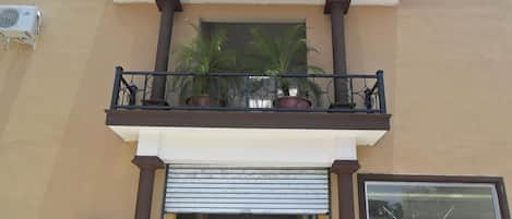 A building with a red and white facade, a balcony with potted plants, and a closed shop entrance.