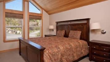 A bedroom with a large bed, wooden headboard, two bedside lamps, and a view of the outdoors through large windows.