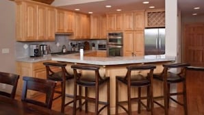 Una cocina con armarios de madera, una isla central con taburetes de bar y electrodomésticos de acero inoxidable.