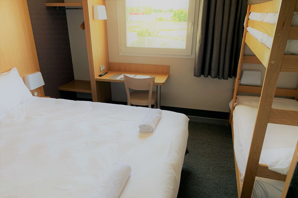Une chambre d’hôtel avec un grand lit, un bureau avec une chaise, un lit superposé et une fenêtre avec des rideaux.