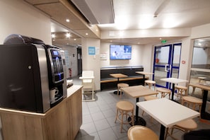 A modern cafe interior with a coffee machine, seating area, and a TV screen on the wall. - Kyriad Direct Clermont Ferrand Nord - Gerzat (Gerzat)