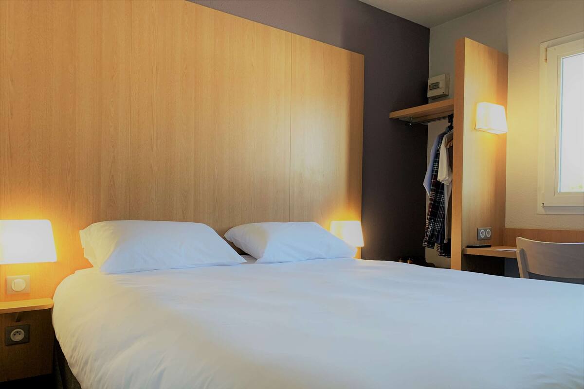 Een netjes opgemaakt bed met witte lakens in een hotelkamer. Aan weerszijden van het bed staan twee bedlampen.
