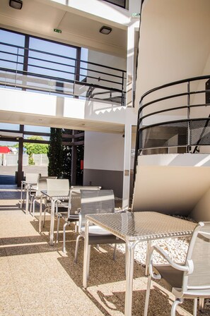A covered outdoor seating area with metal tables and chairs, a staircase, and a view of the street. - Kyriad Direct Clermont Ferrand Nord - Gerzat (Gerzat)