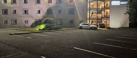 Un parking avec une voiture blanche garée devant un bâtiment portant l’inscription « Kyriad DIRECT ».