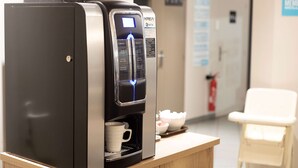 A coffee machine with a digital display, a cup holder, and a tray with cups and a bowl. - Kyriad Direct Clermont Ferrand Nord - Gerzat (Gerzat)
