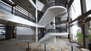 A multi-level atrium with a central staircase, outdoor seating area with tables and chairs, and a view of the surrounding landscape. - Kyriad Direct Clermont Ferrand Nord - Gerzat (Gerzat)