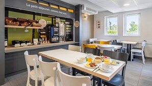 A breakfast area with a counter displaying pastries and beverages, tables with breakfast items, and a view of greenery outside. - B&B HOTEL Poitiers (1) (Chasseneuil-du-Poitou)
