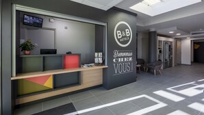 A modern hotel reception desk with a digital screen, a welcome sign, and a plant. - B&B HOTEL Poitiers (1) (Chasseneuil-du-Poitou)