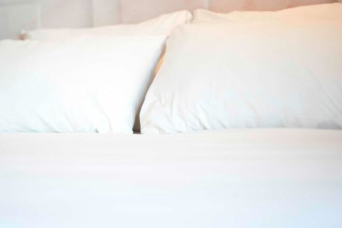 Un lit avec du linge de lit et des oreillers blancs.