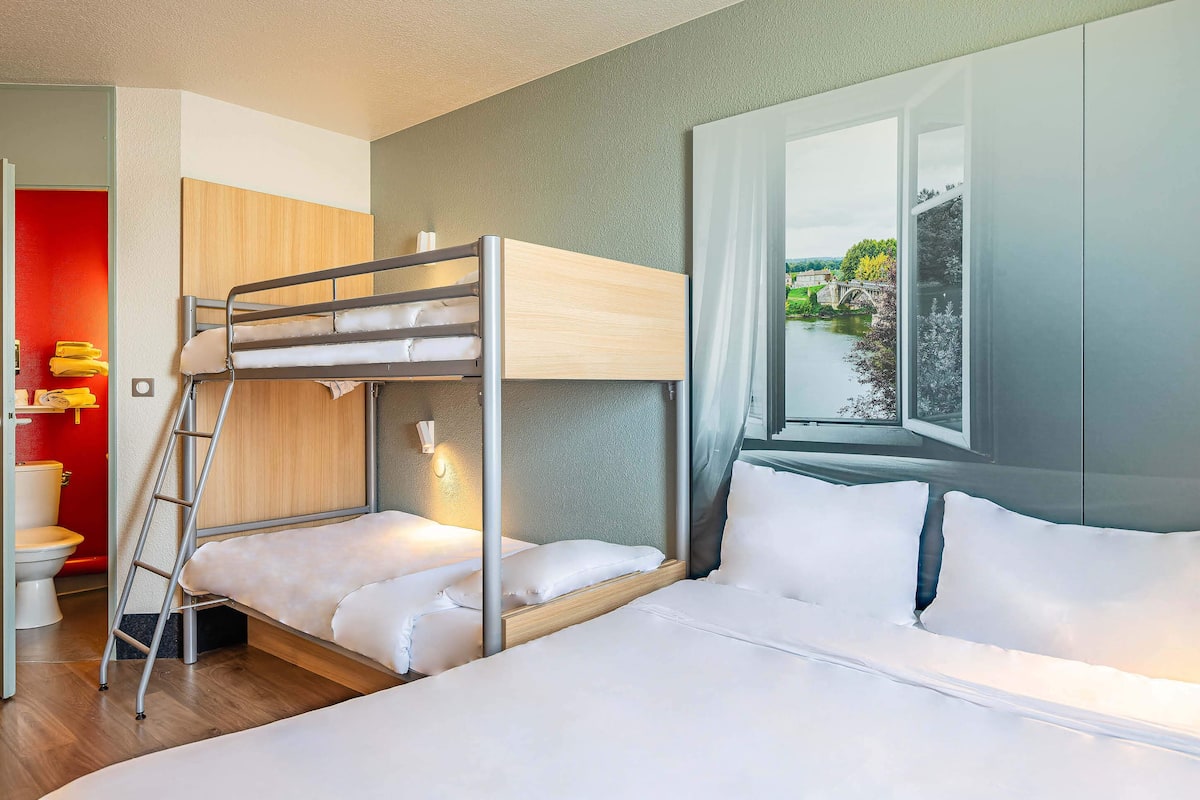 A bunk bed room with a wooden headboard, a ladder, and a window with a view of greenery.