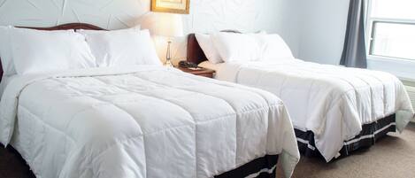 A hotel room with two beds, a nightstand, a lamp, and a framed picture on the wall.