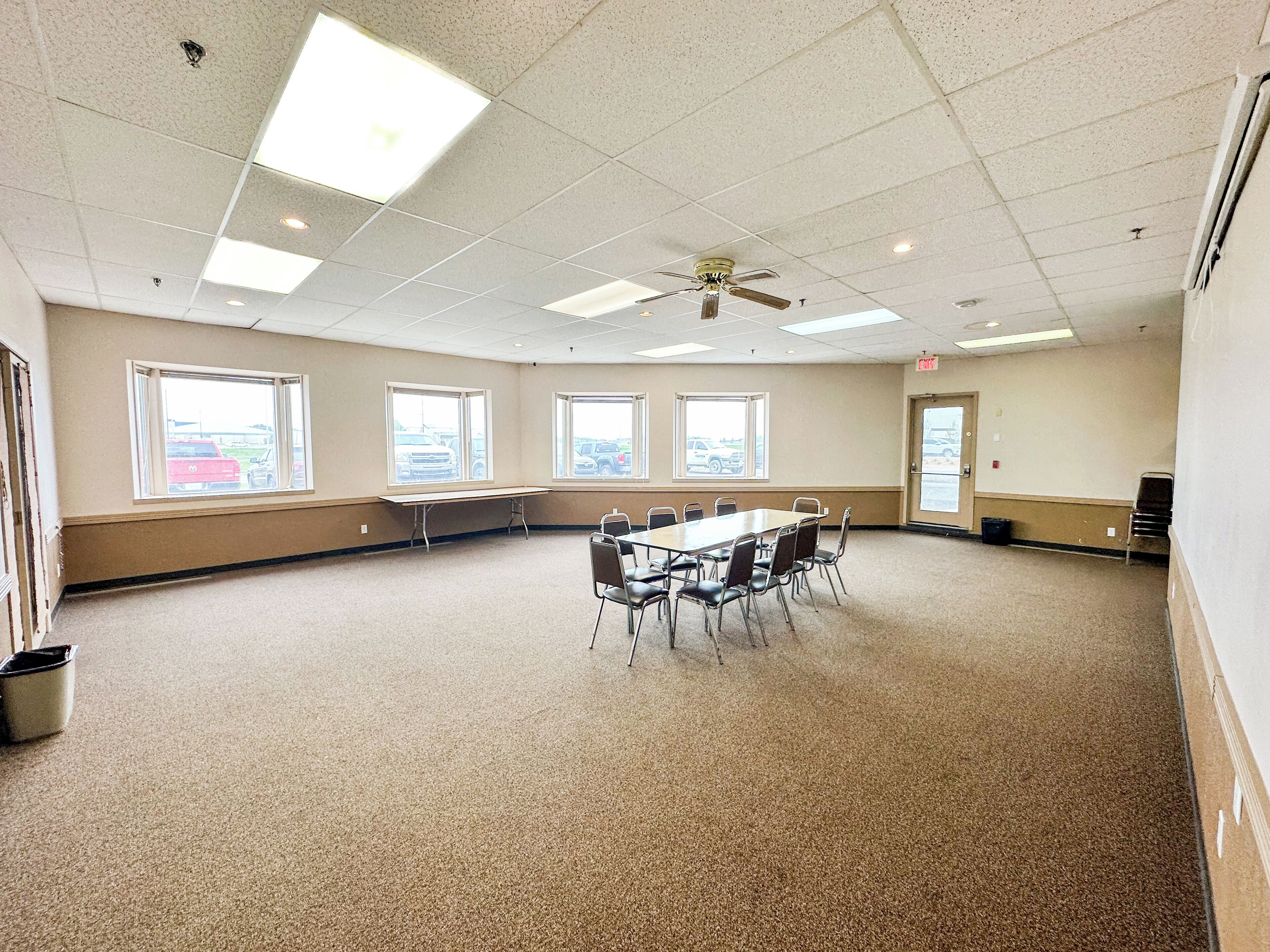 A conference room with a long table, chairs, windows, and a ceiling fan.