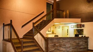 Una escalera con barandillas de madera que conduce a una zona de recepción con mostrador de piedra y cuadros enmarcados en la pared.