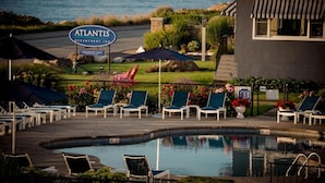 Ein Poolbereich mit Liegestühlen, ein Schild für Atlantis Oceanfront Inn und Blick auf den Ozean.