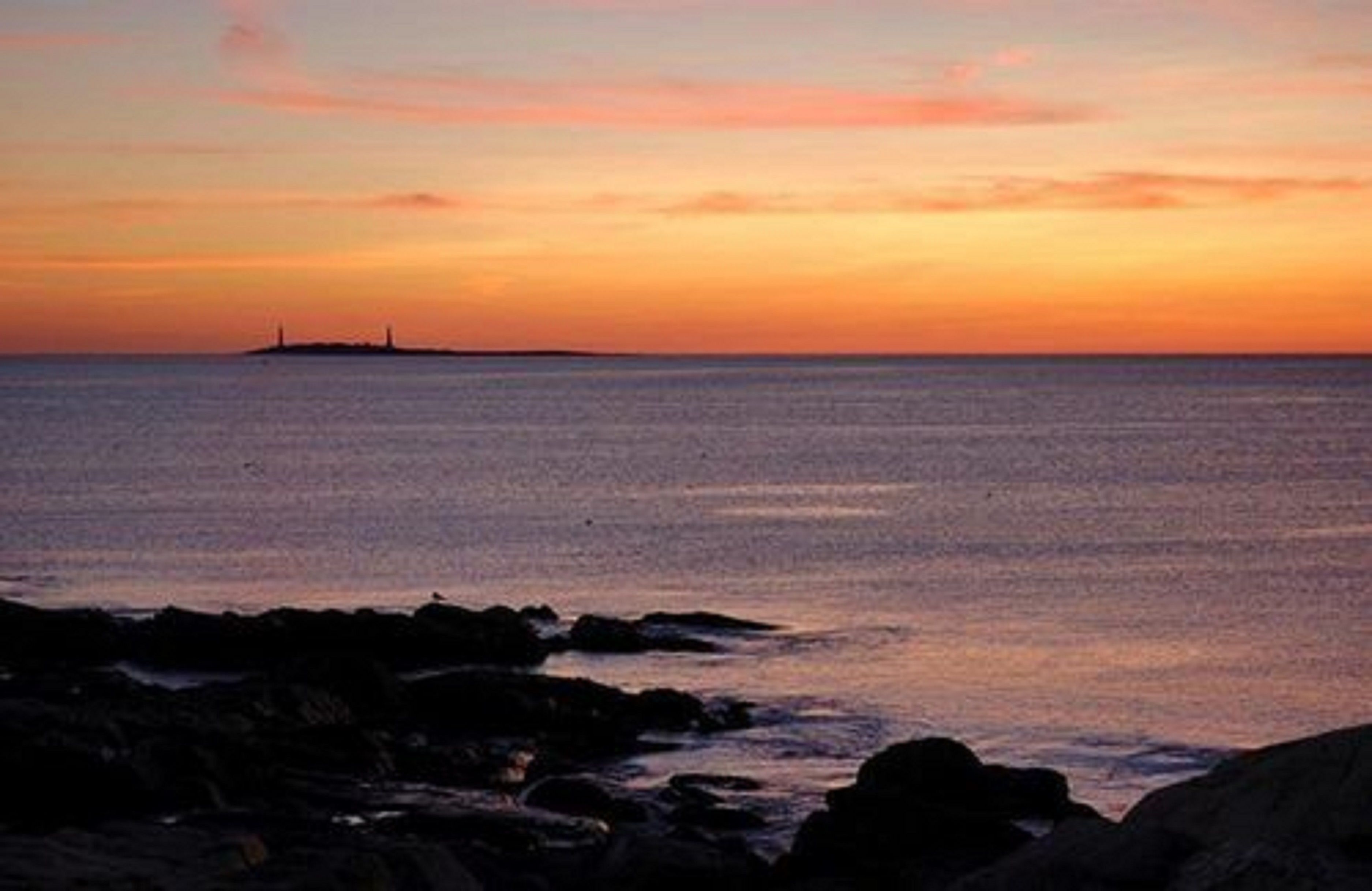 A coastal sunset with rocky shoreline and distant landmass.