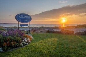 A sign for 'Atlantis Oceanfront Inn' with a view of the sunset over the ocean.