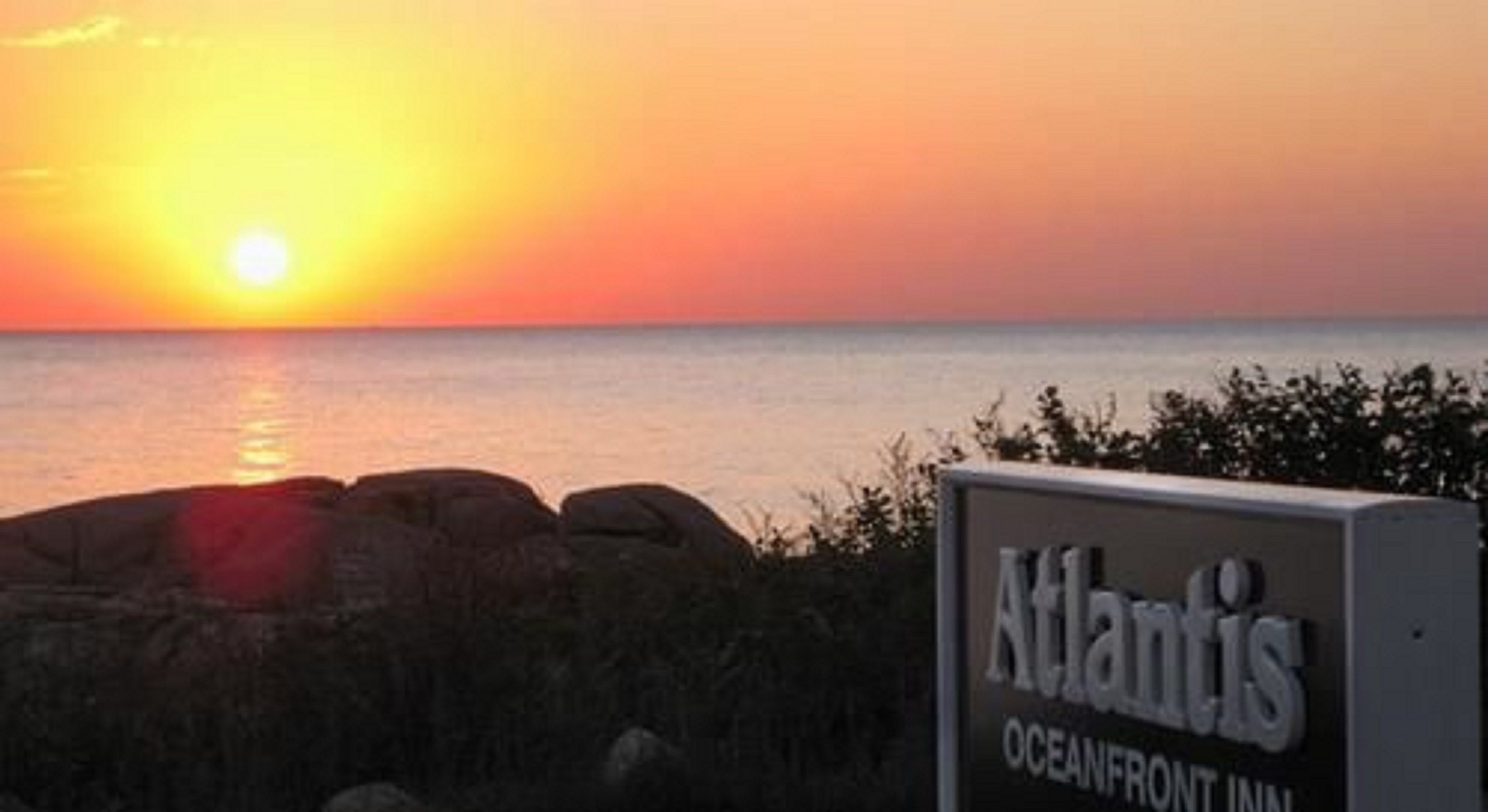 A sunset view with a sign for 'Atlantis Oceanfront Inn'.