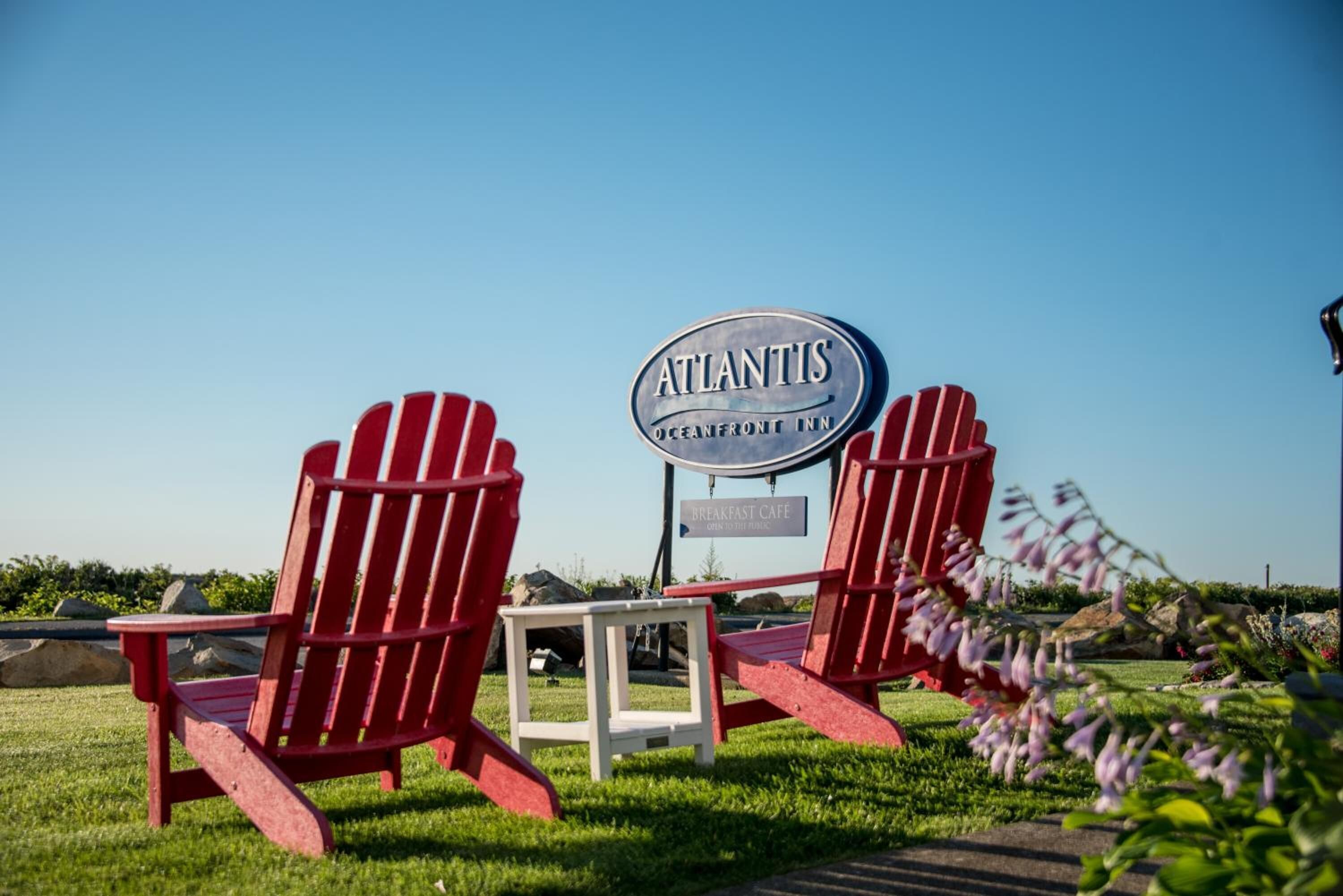 Two red Adirondack chairs, a sign for 'Atlantis Oceanfront Inn', and a 'Breakfast Cafe' sign.