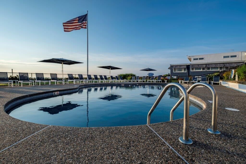 Une piscine avec un drapeau, des chaises longues et un bâtiment en arrière-plan.