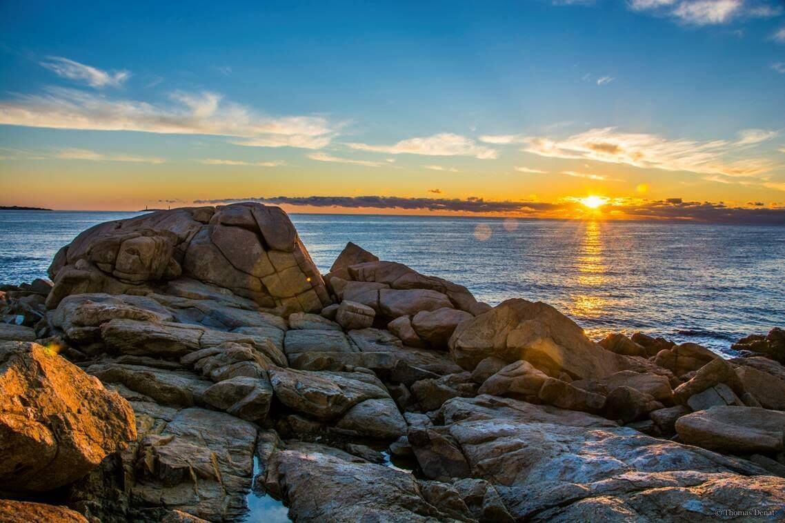 Un littoral rocheux, parsemé de gros rochers, avec un coucher de soleil sur l’océan.