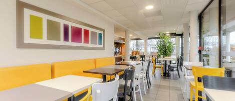 Interior de restaurante moderno con asientos amarillos y blancos, un ventanal grande y un techo con diseño de cuadrícula.