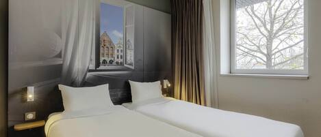 A hotel room with a large bed, a window with curtains, and a view of a building outside.