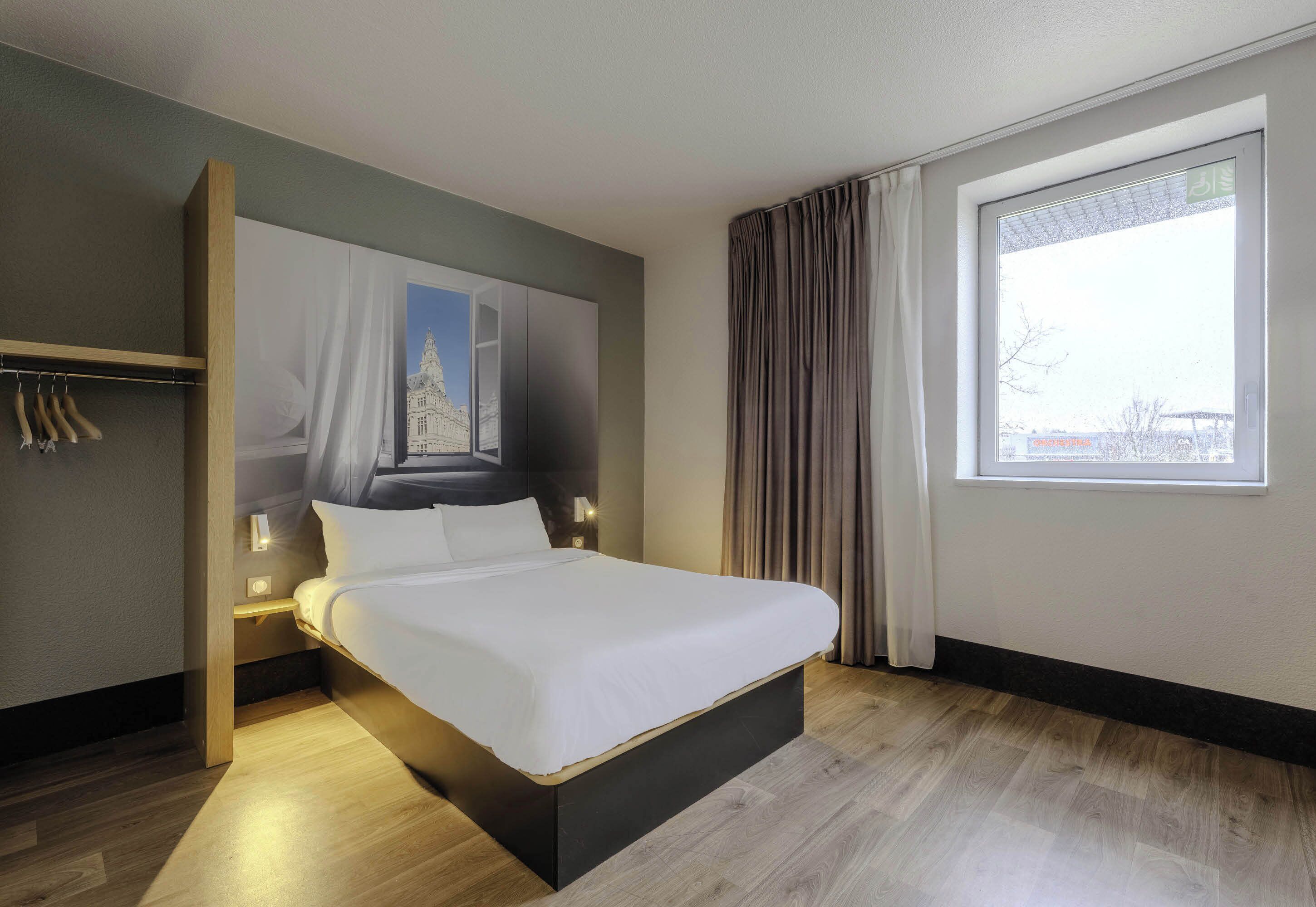 Una camera d'albergo moderna con un letto grande, un comodino, un armadio e una finestra con tende.