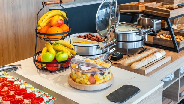 Un bufé con diversas opciones de comida, incluyendo frutas, yogur y pan.