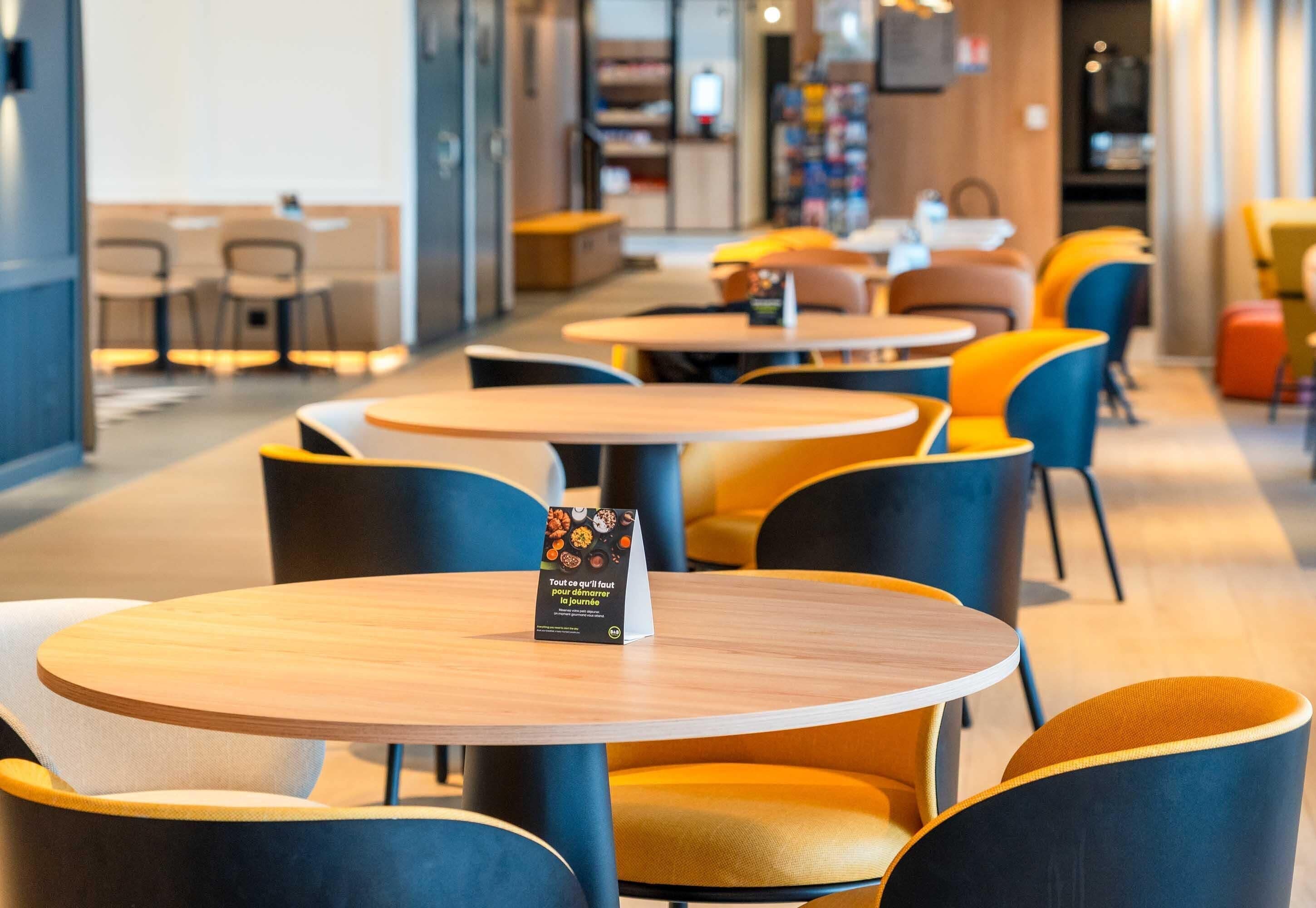 A modern cafe with round tables and yellow and blue chairs.