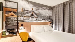 Una habitación de hotel con cama, escritorio con silla, cafetera y espejo.
