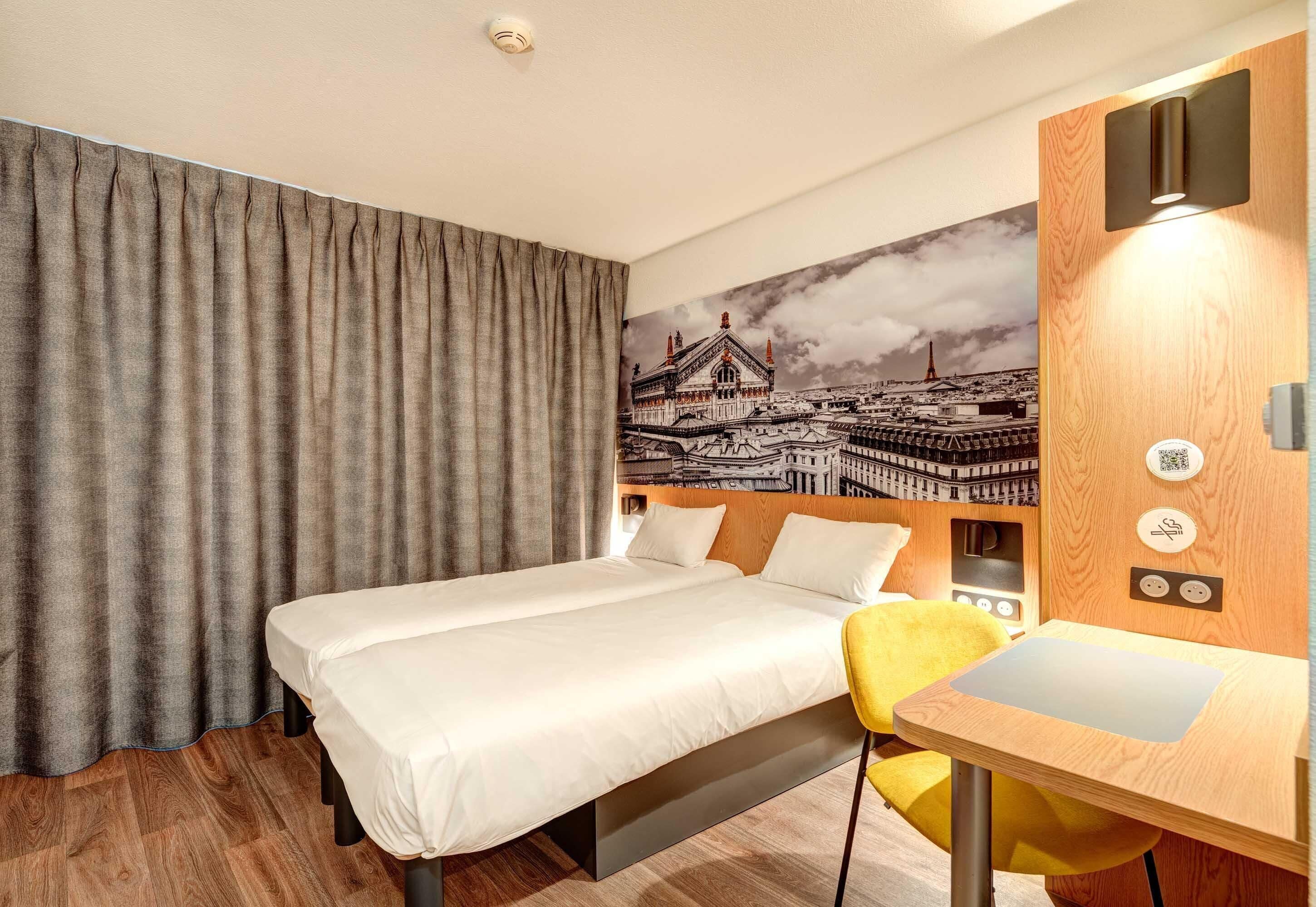 Una habitación de hotel con cama, escritorio, silla, cortina y un mural en la pared.