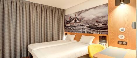 Una habitación de hotel con cama, escritorio, silla, cortina y un mural en la pared.