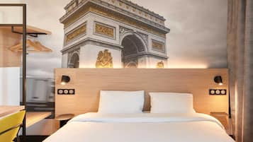 Une chambre d’hôtel comprenant un lit, des lampes de chevet, une tête de lit en bois, un bureau avec une chaise et une fresque murale représentant l’Arc de Triomphe.