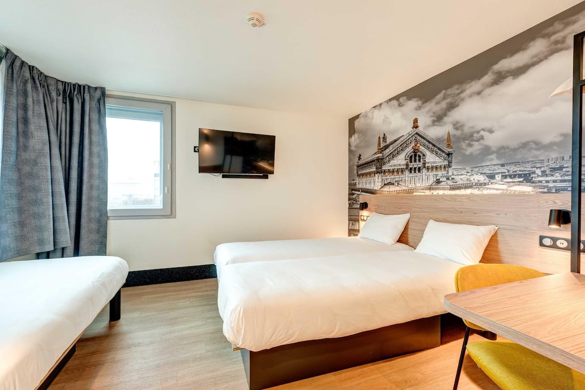 A hotel room with two beds, a TV, a wooden table, and a large wall mural.