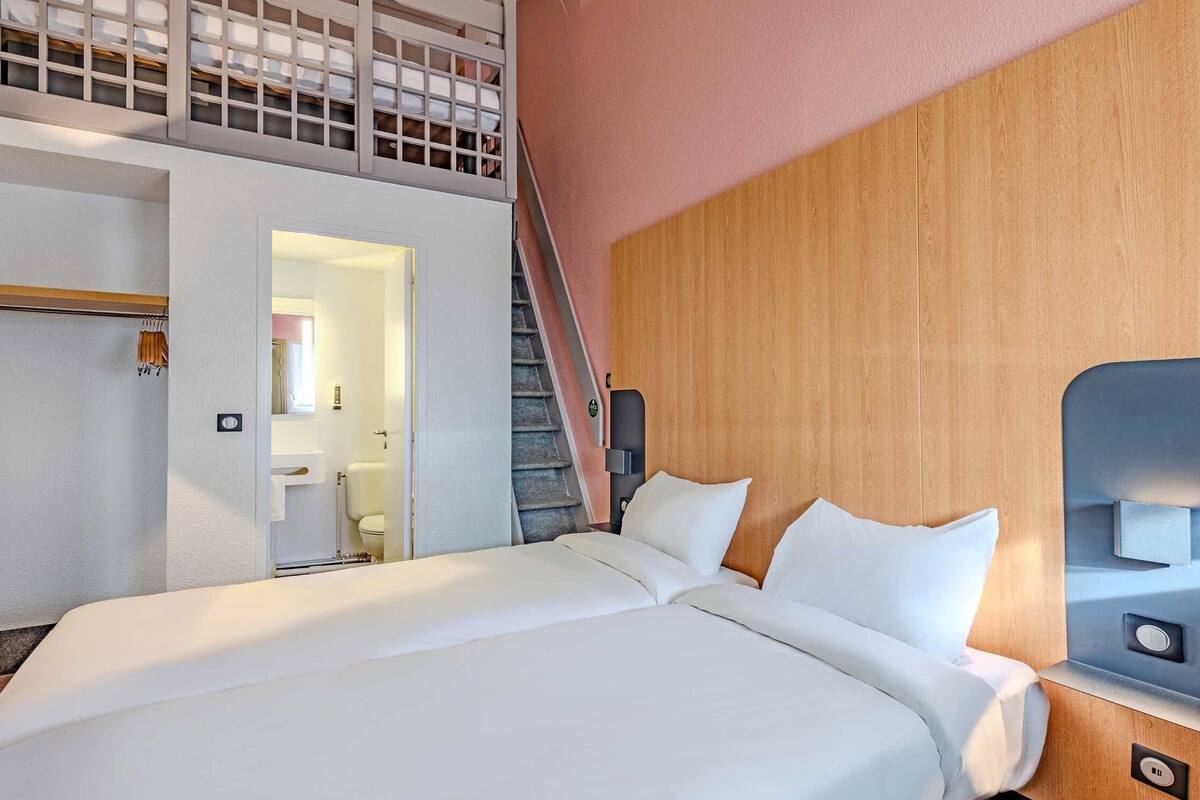 A modern hotel room with a large bed, wooden headboard, and a staircase leading to an upper level.