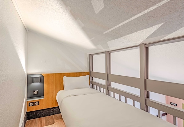 A compact hotel room with a single bed, a small bedside table, a power outlet, and a window with a view.