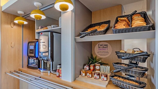 A breakfast station with a coffee machine, baskets of pastries, and condiments. - B&B HOTEL Brest Kergaradec (Gouesnou)